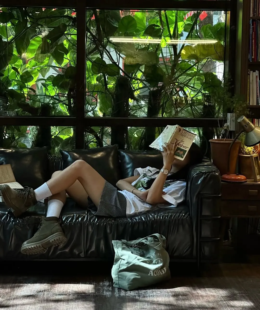 Person reading on a leather sofa surrounded by plants