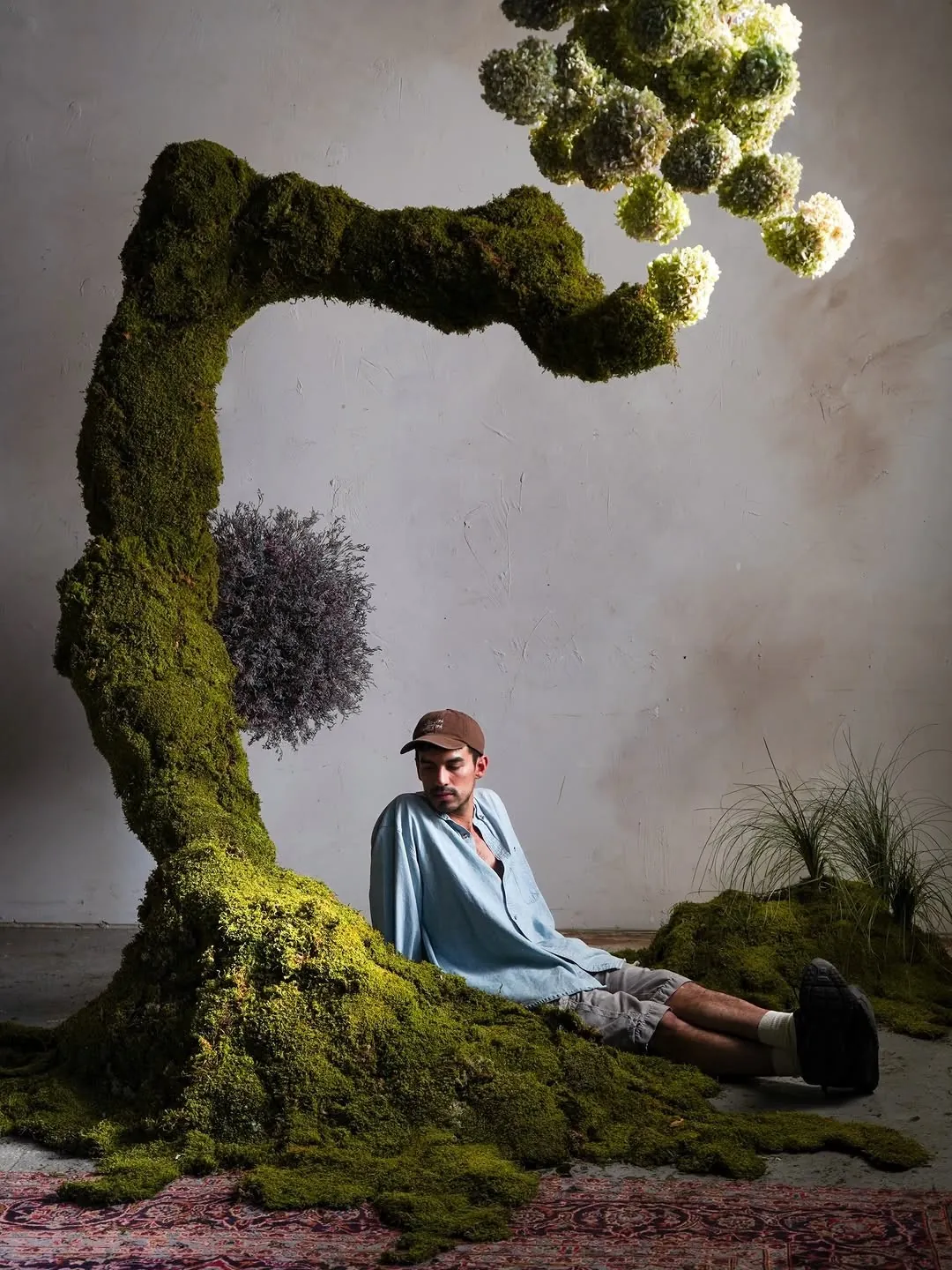 Person resting beneath a moss-covered tree sculpture